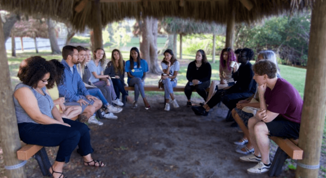 A circle of learners in conversation under an outdoor pavilion